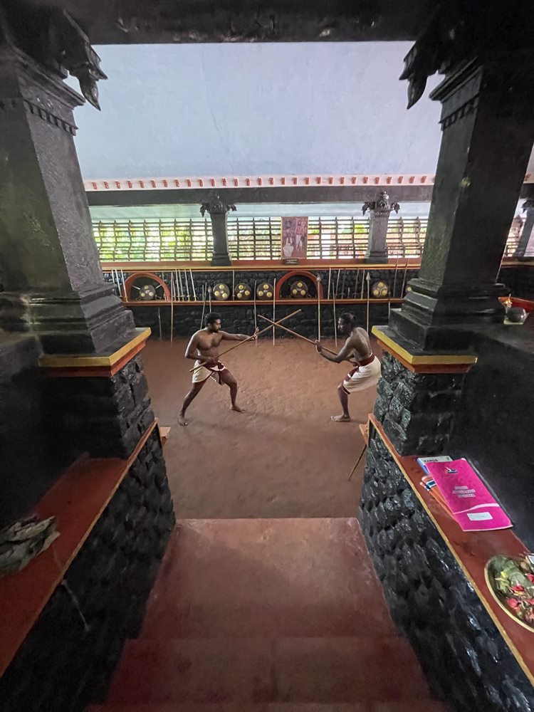 Sparring with staves seen from the steps between the Kalari pillars
