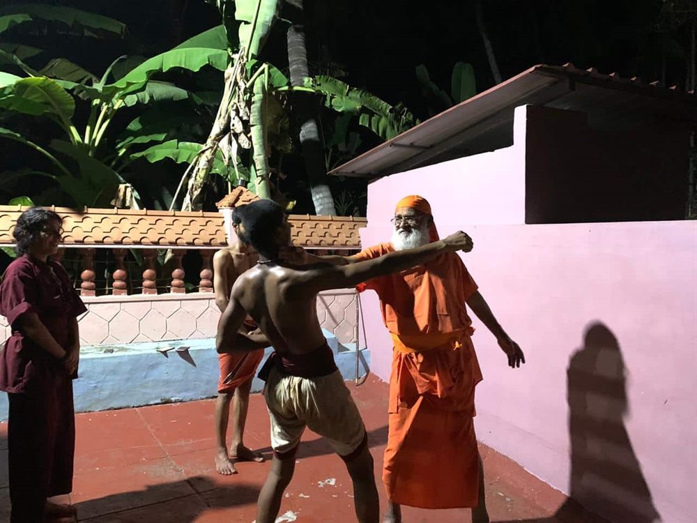 A student striking with a long staff as Guruji meets the blow